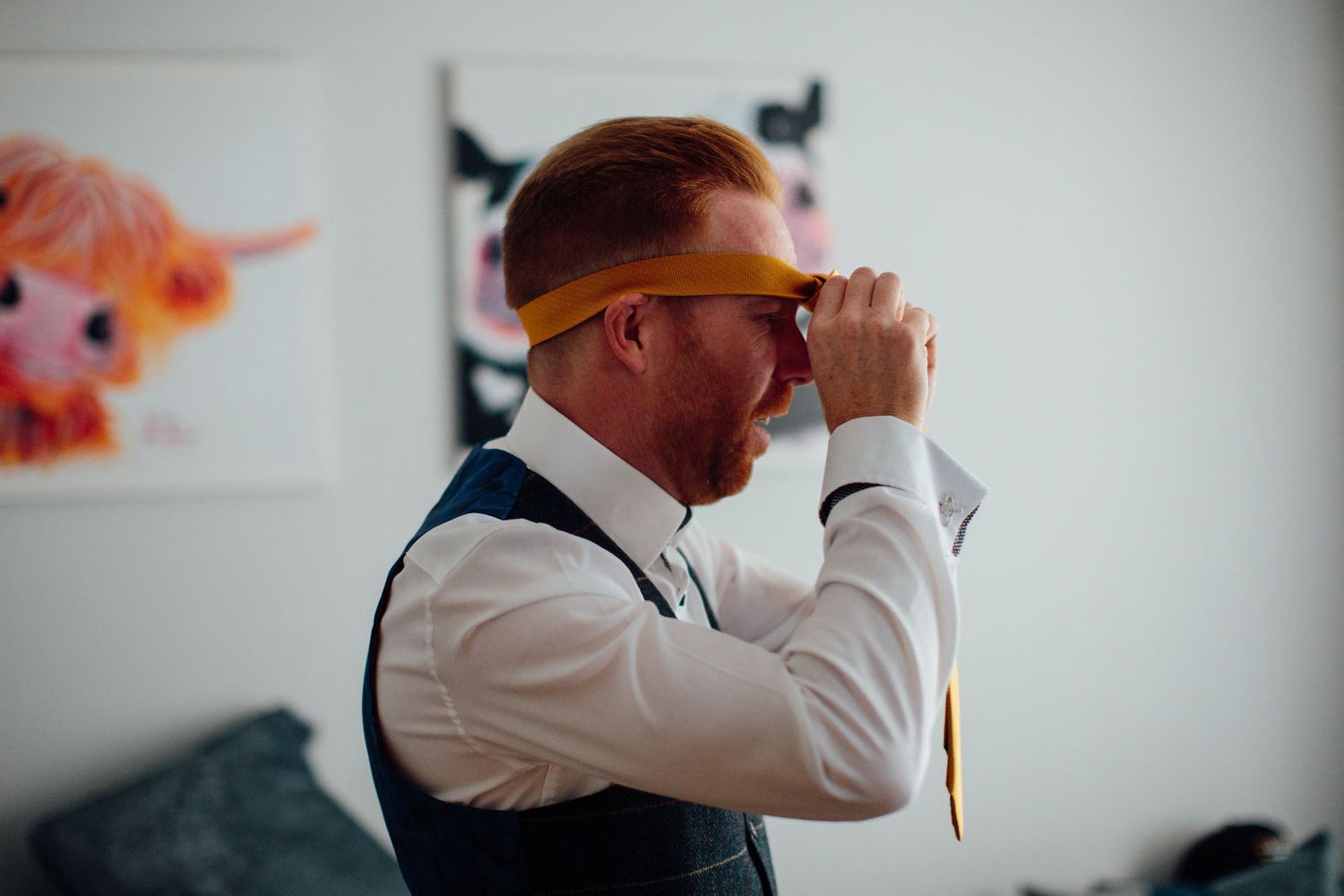 A person in formal attire adjusting a gold tie while getting ready.