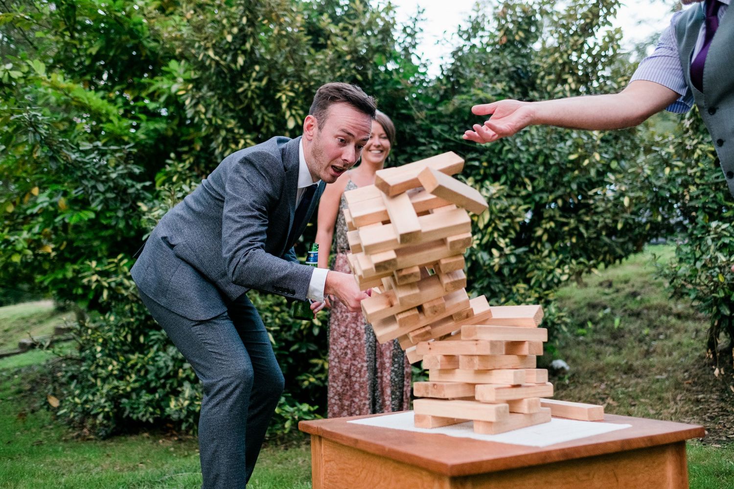 Giant wooden Jenga blocks tumble during an outdoor wedding reception game.