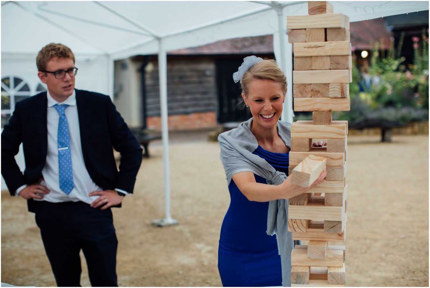 Players in formal attire carefully removing blocks from giant Jenga tower at outdoor event.