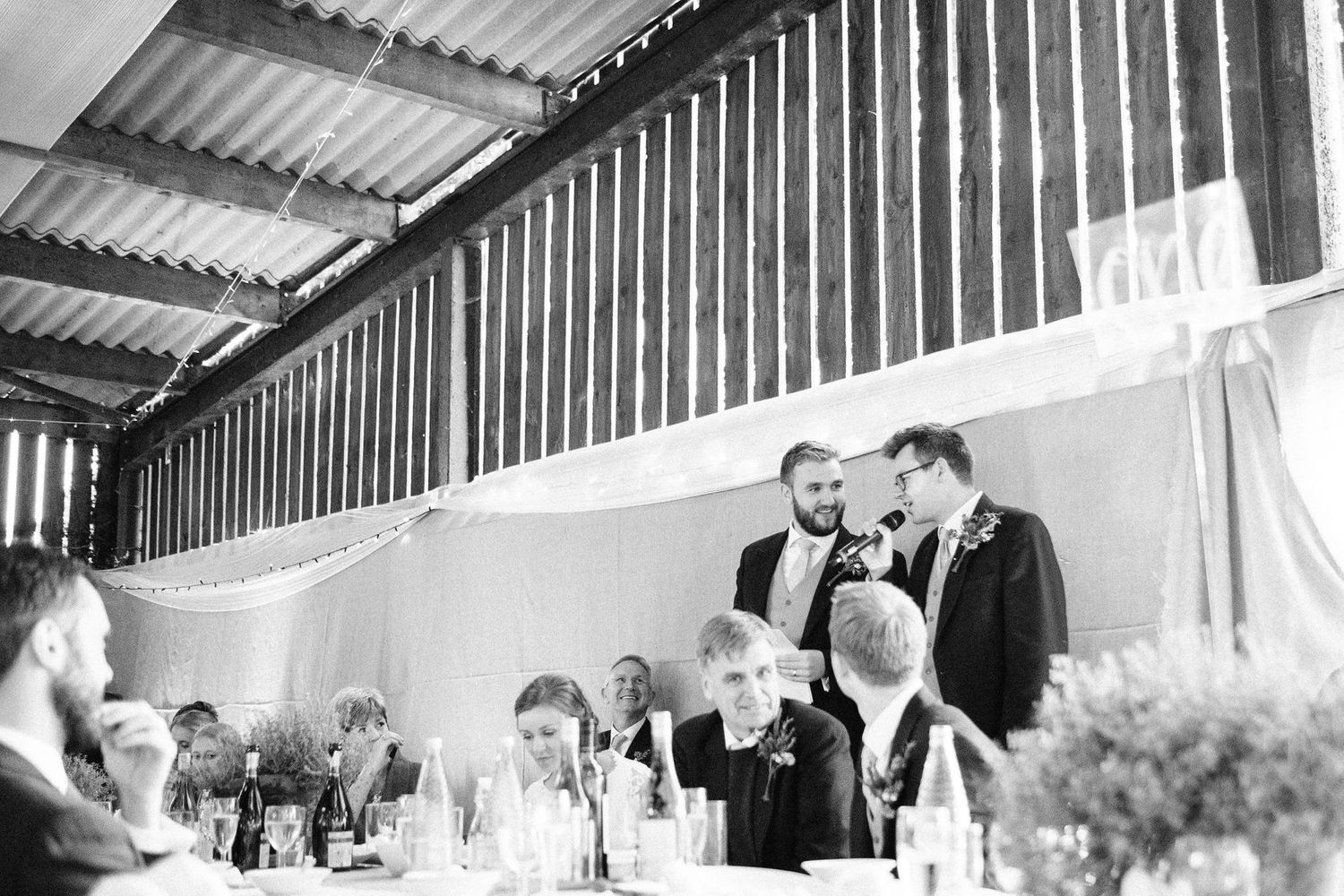 Black and white photo of guests seated under a covered outdoor reception area.