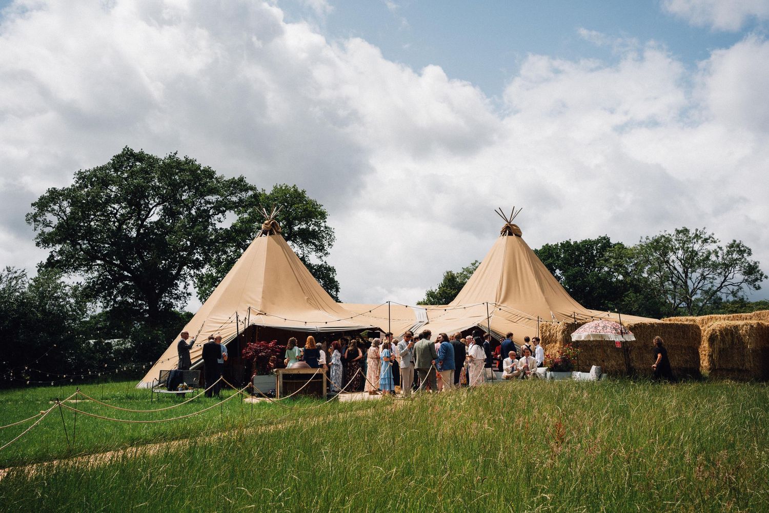 Large beige tipi-style tents set up in a grassy field for an outdoor event.