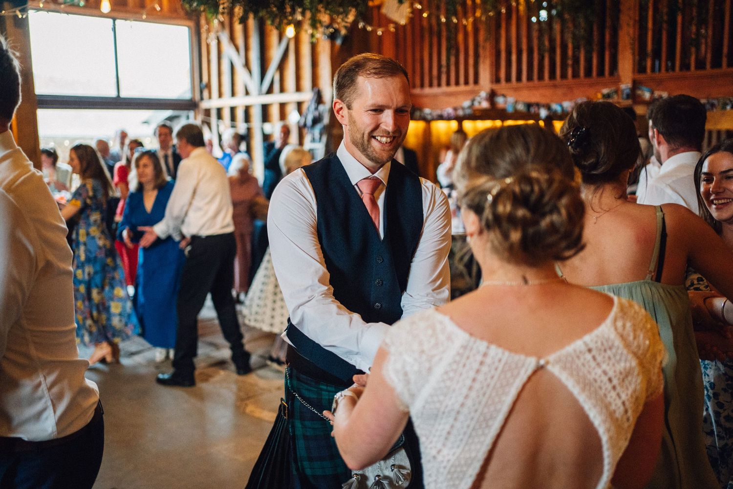 Joyful dancing and celebration at rustic barn wedding reception under warm lighting.