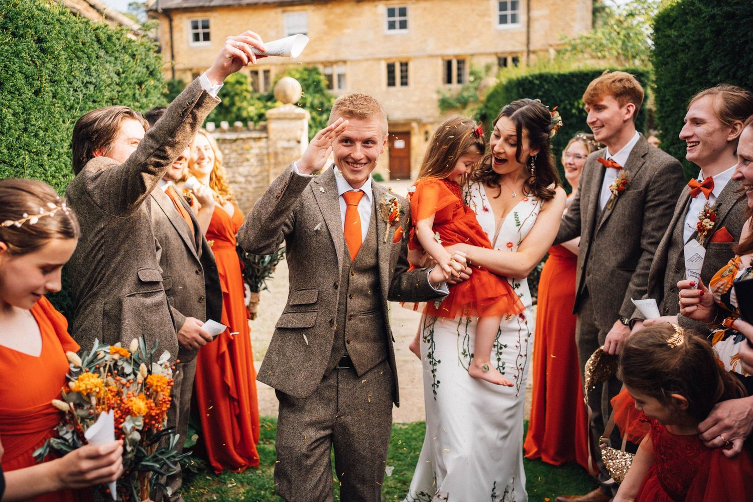 Wedding party celebrates with orange and gray color scheme in outdoor garden setting.