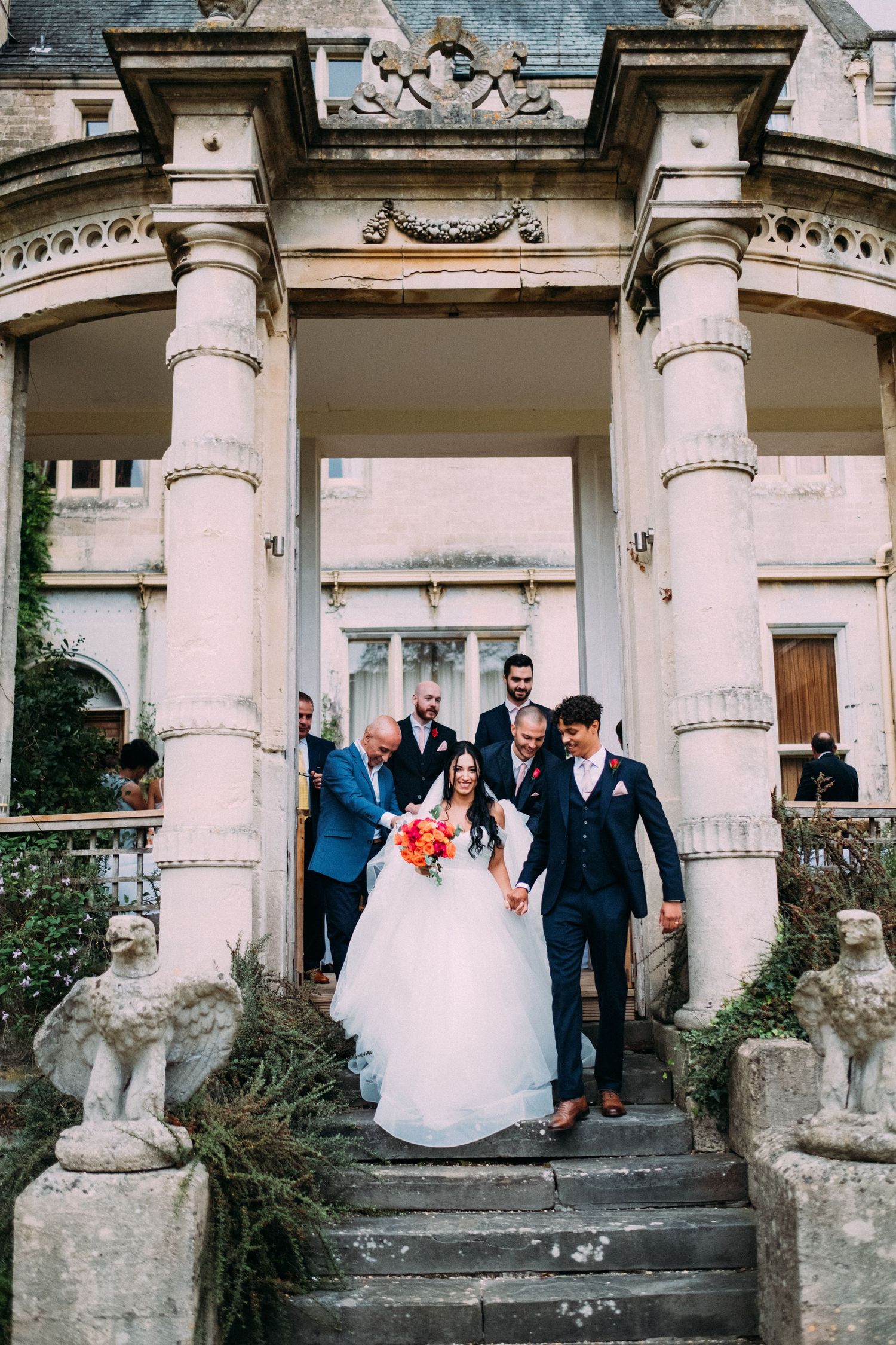 Wedding party descending stone steps of a classical columned entrance to a historic building.