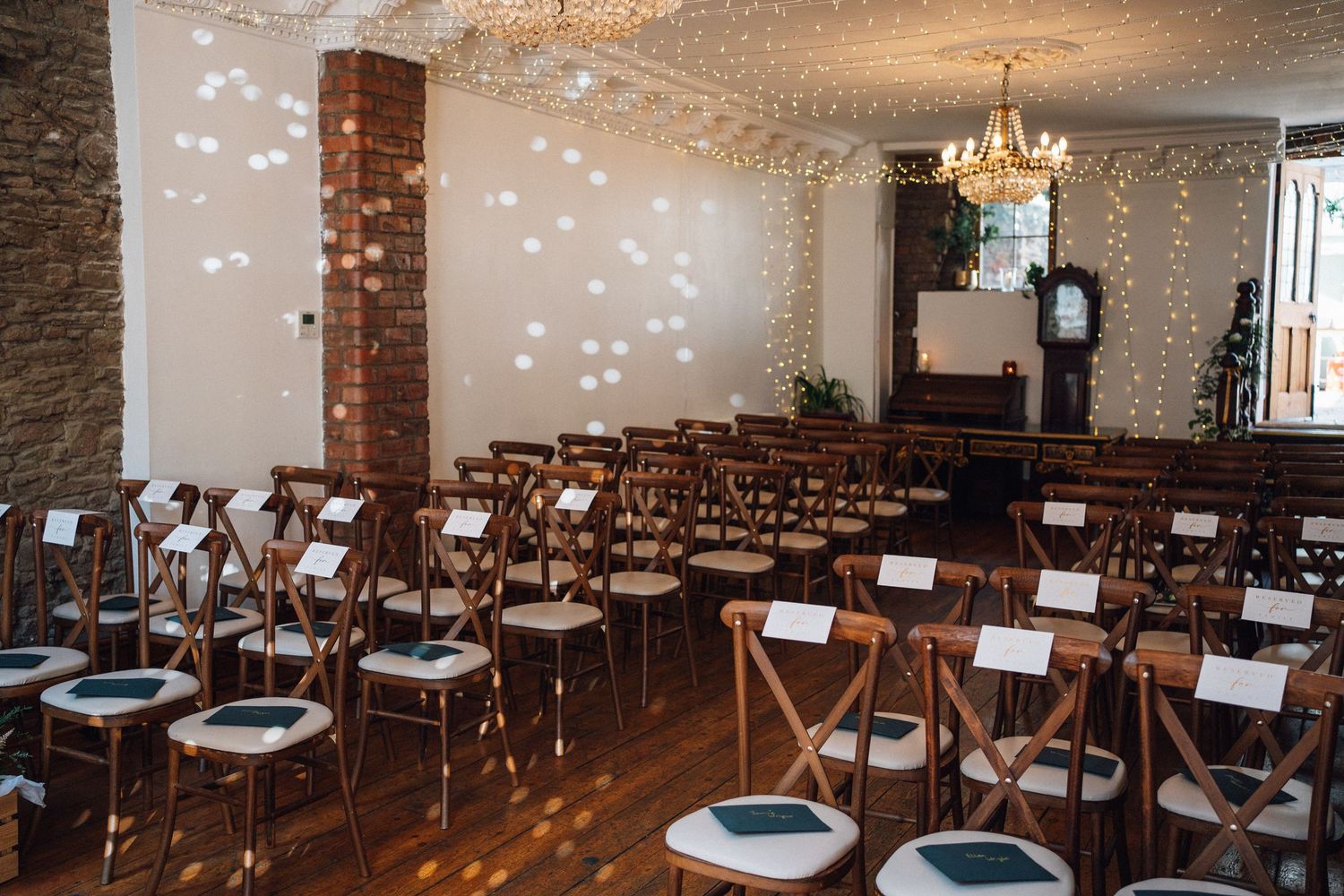 Elegant wedding reception venue with exposed brick walls, crystal chandeliers, and wooden chairs arranged in rows.