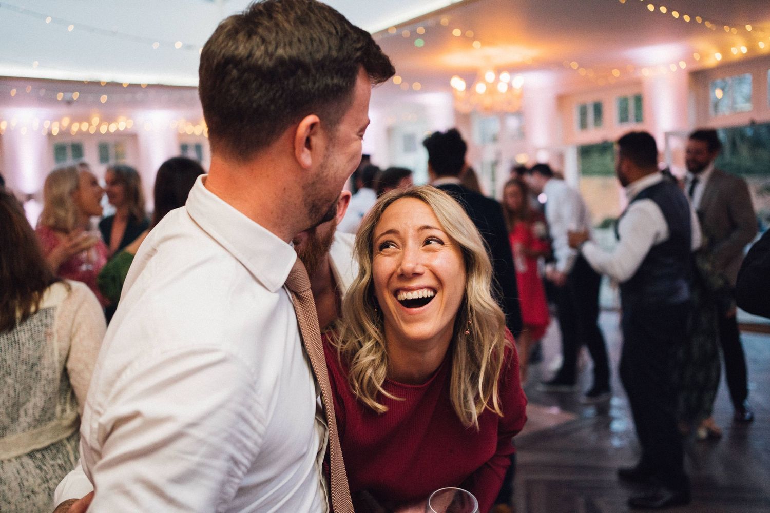Candid moments of laughter and dancing captured at a wedding reception under twinkling lights and a white tent.