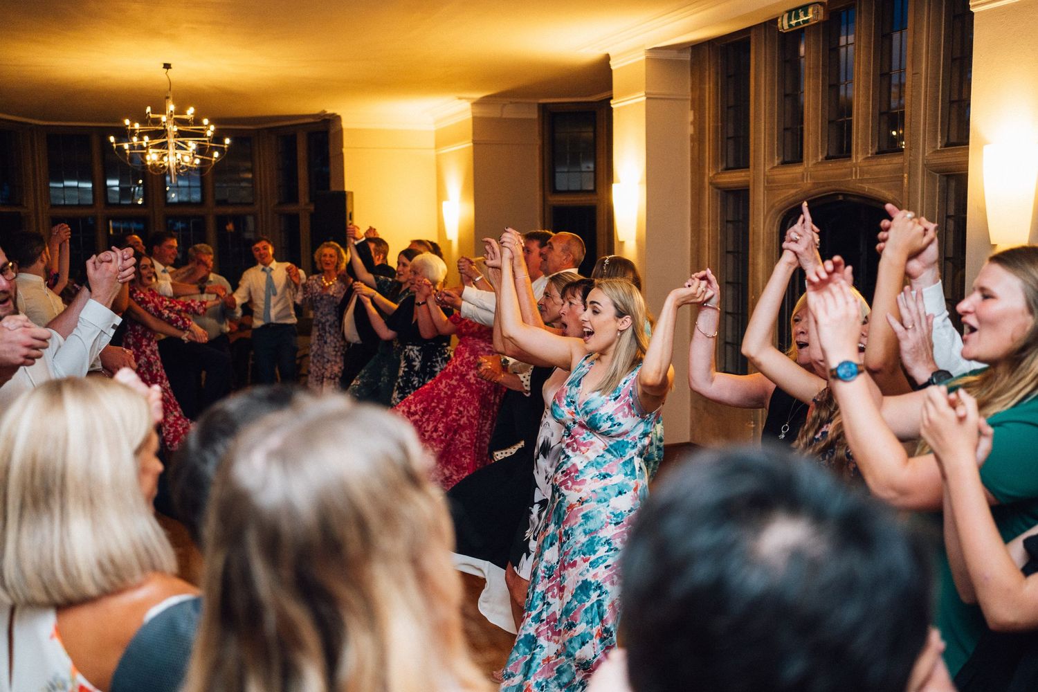 Guests dancing and celebrating at an indoor wedding reception with golden ambient lighting.