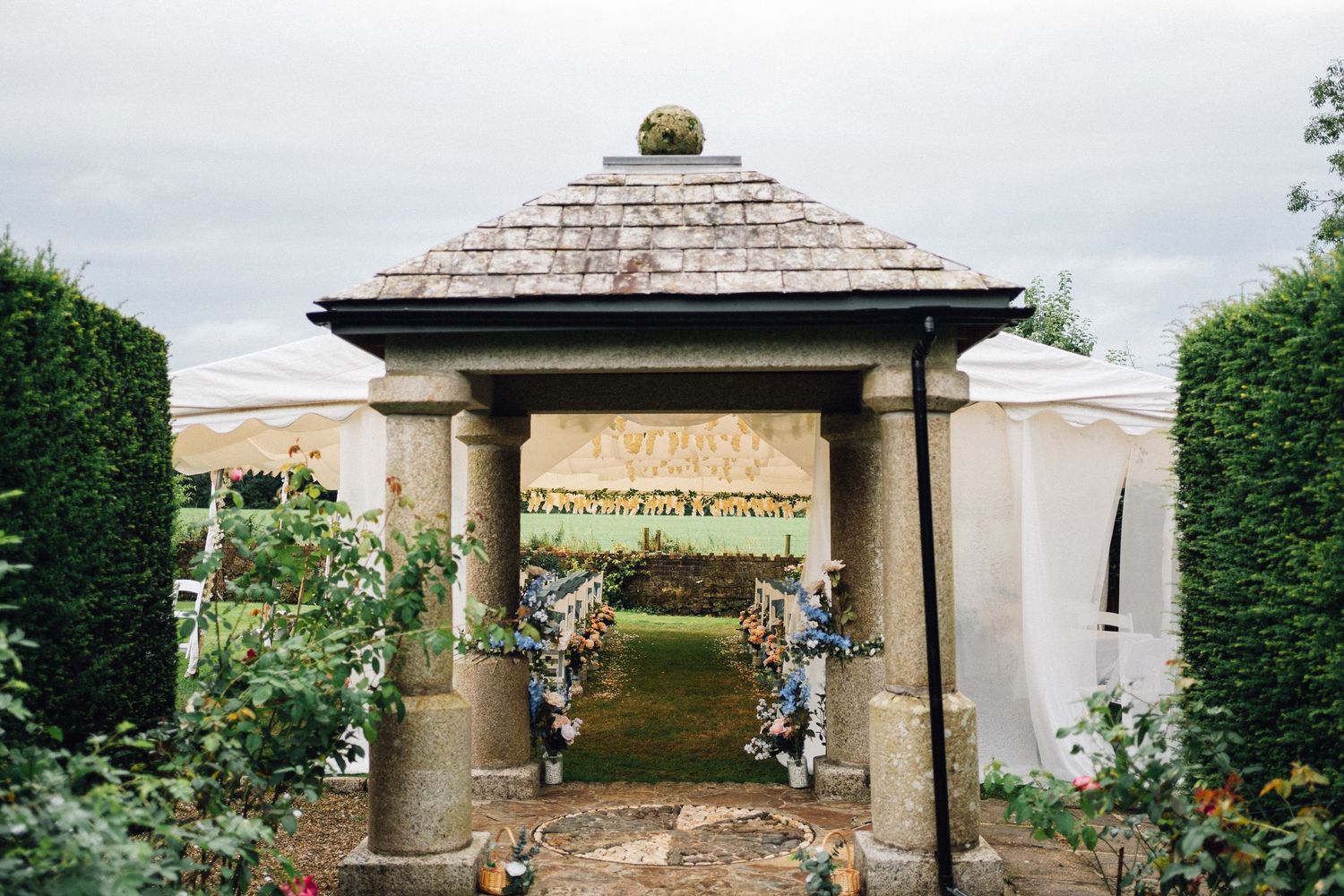 Elegant outdoor wedding gazebo decorated with white draping and floral arrangements in a garden setting.