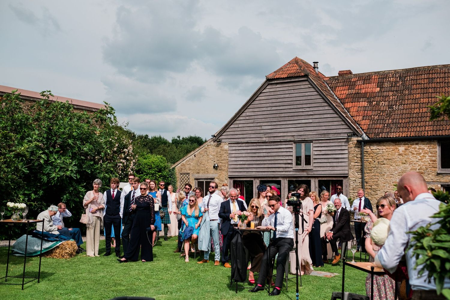 Wedding celebration taking place outside a traditional stone barn with guests mingling on the lawn.