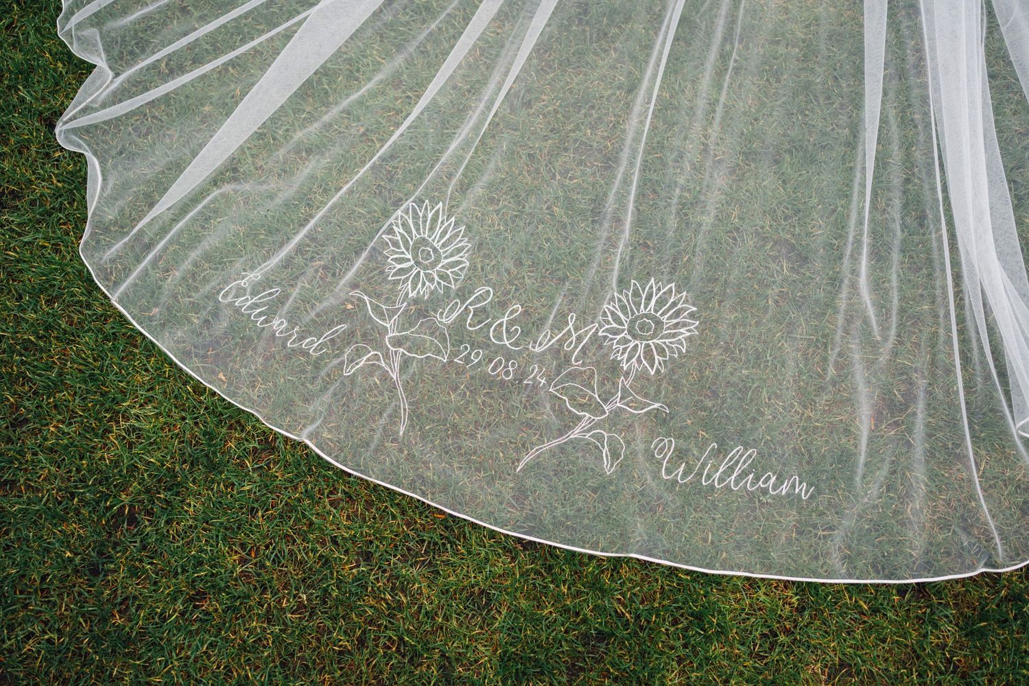 Delicate lace and embroidered details on a white tulle wedding veil laid out on grass.