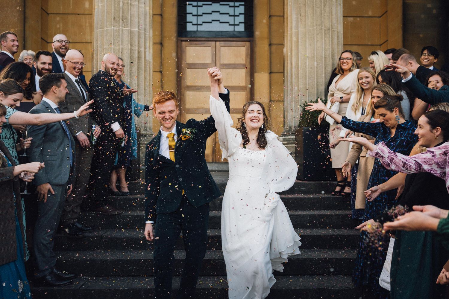 Wedding celebration on stone steps with confetti being thrown in celebration.