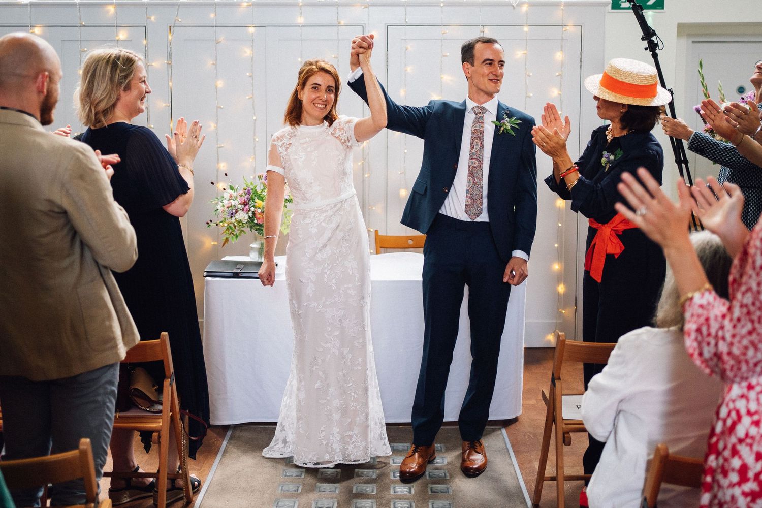 Wedding guests dancing and celebrating during a joyful reception with pink floral decorations in the background.