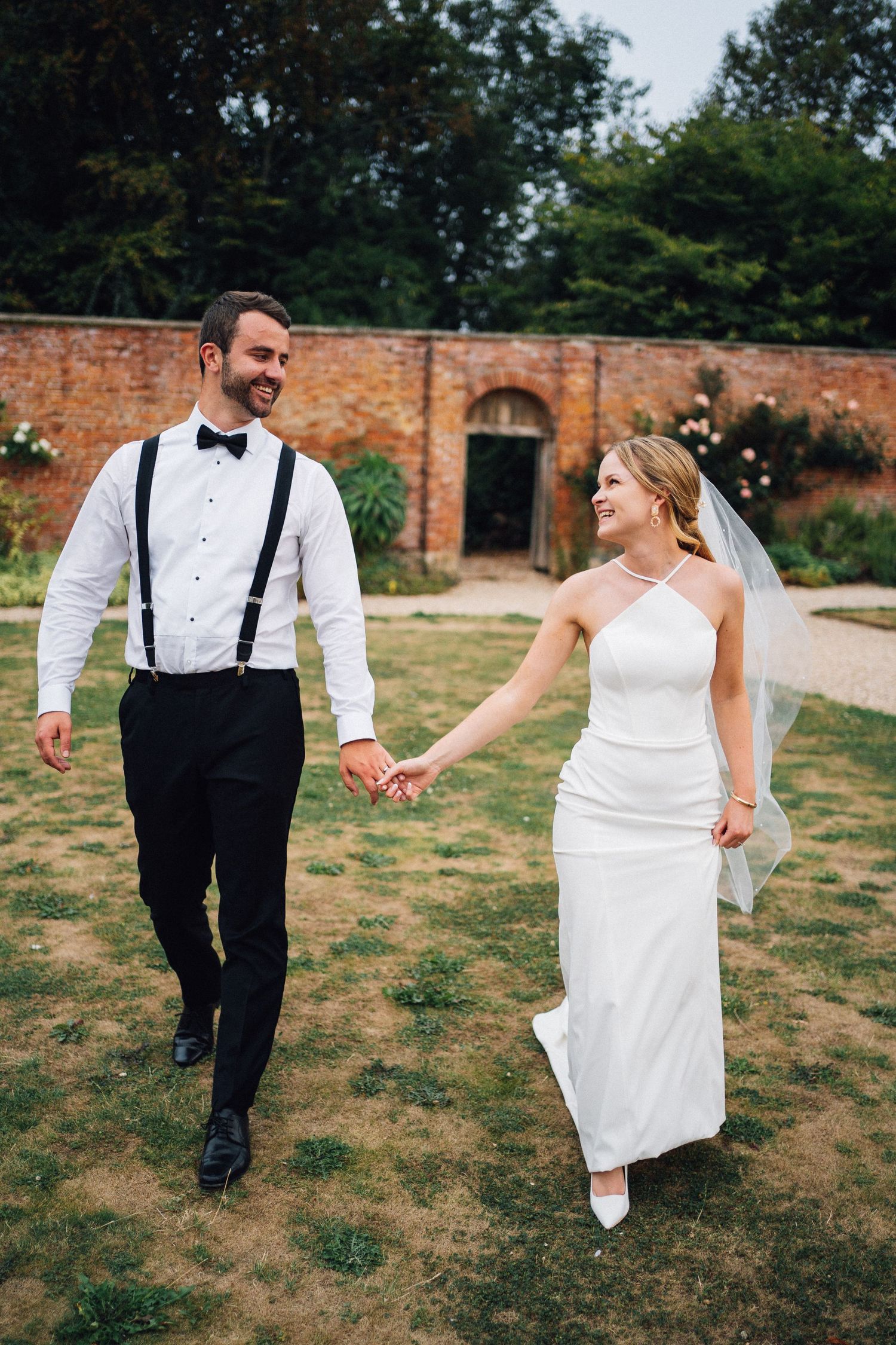 A couple walking hand in hand on their wedding day in a walled garden setting.