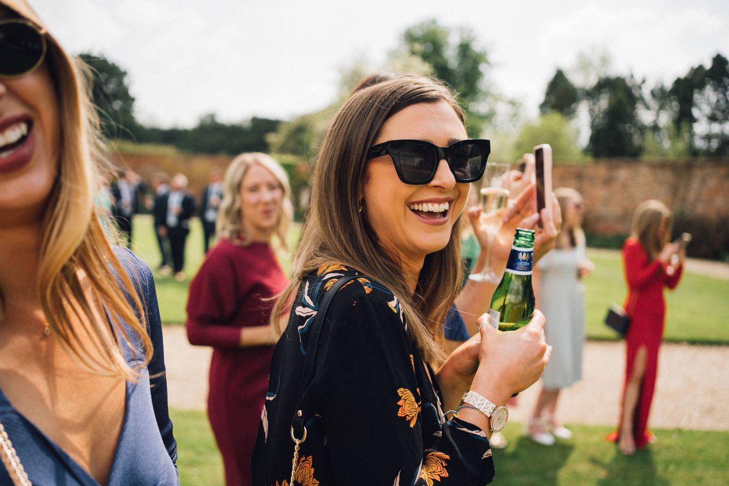 People enjoying drinks and laughing at an outdoor social gathering on a sunny day.