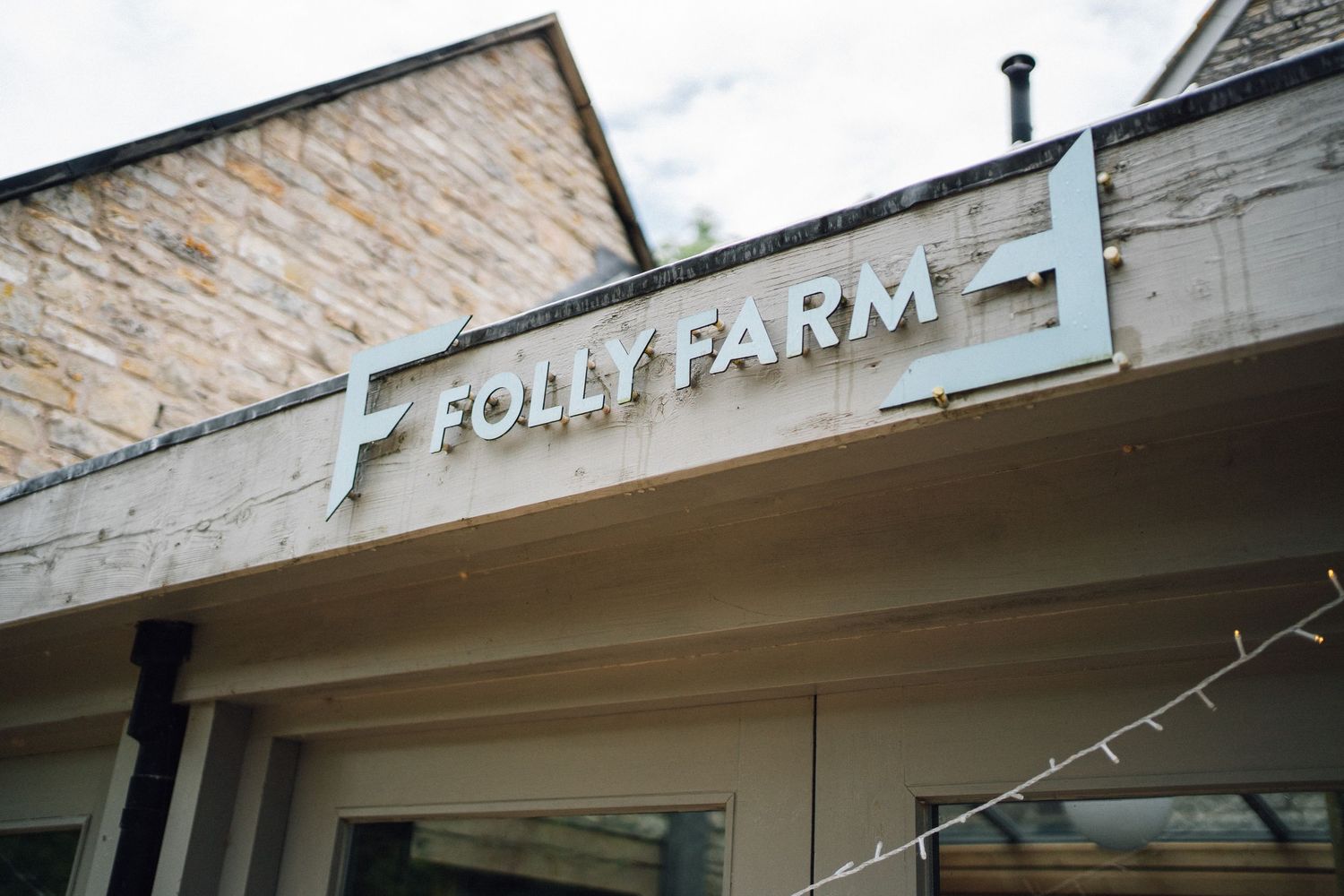 Folly Farm sign mounted on exterior wall of rustic stone and wood building entrance.