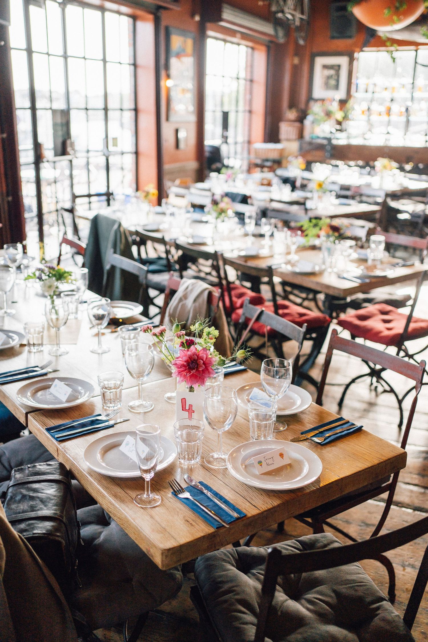Elegant restaurant dining room with wooden tables set for a wedding reception, featuring pink flowers and blue napkins.