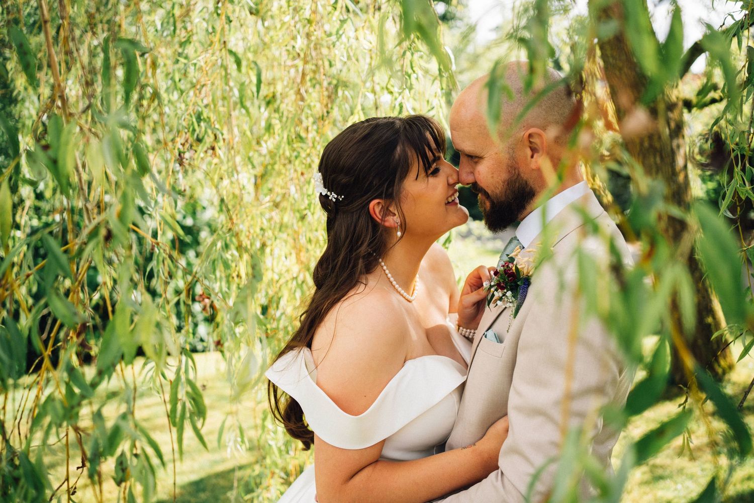 Romantic wedding portraits captured among drooping willow tree branches in natural lighting.