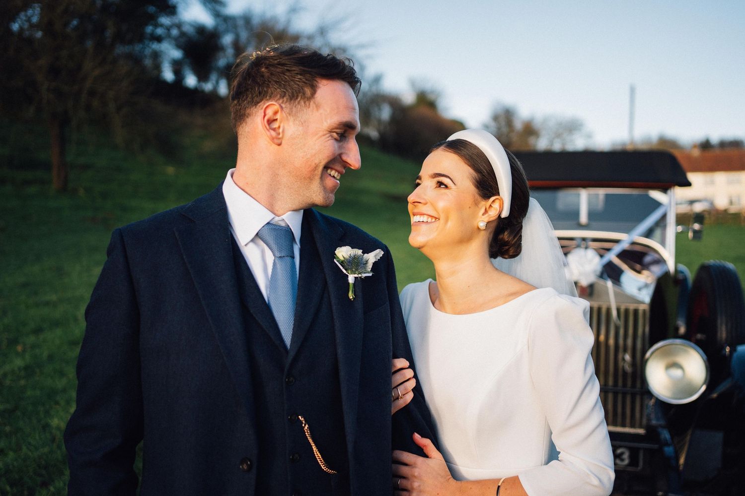 A happy couple shares joyful moments together on their wedding day with a vintage car in the background.