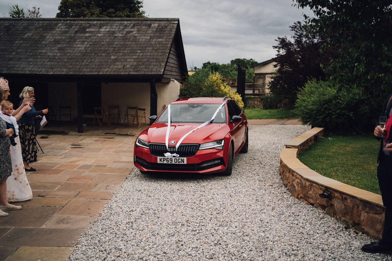 A red Tesla car parked outside a rustic wedding venue on a stone driveway.