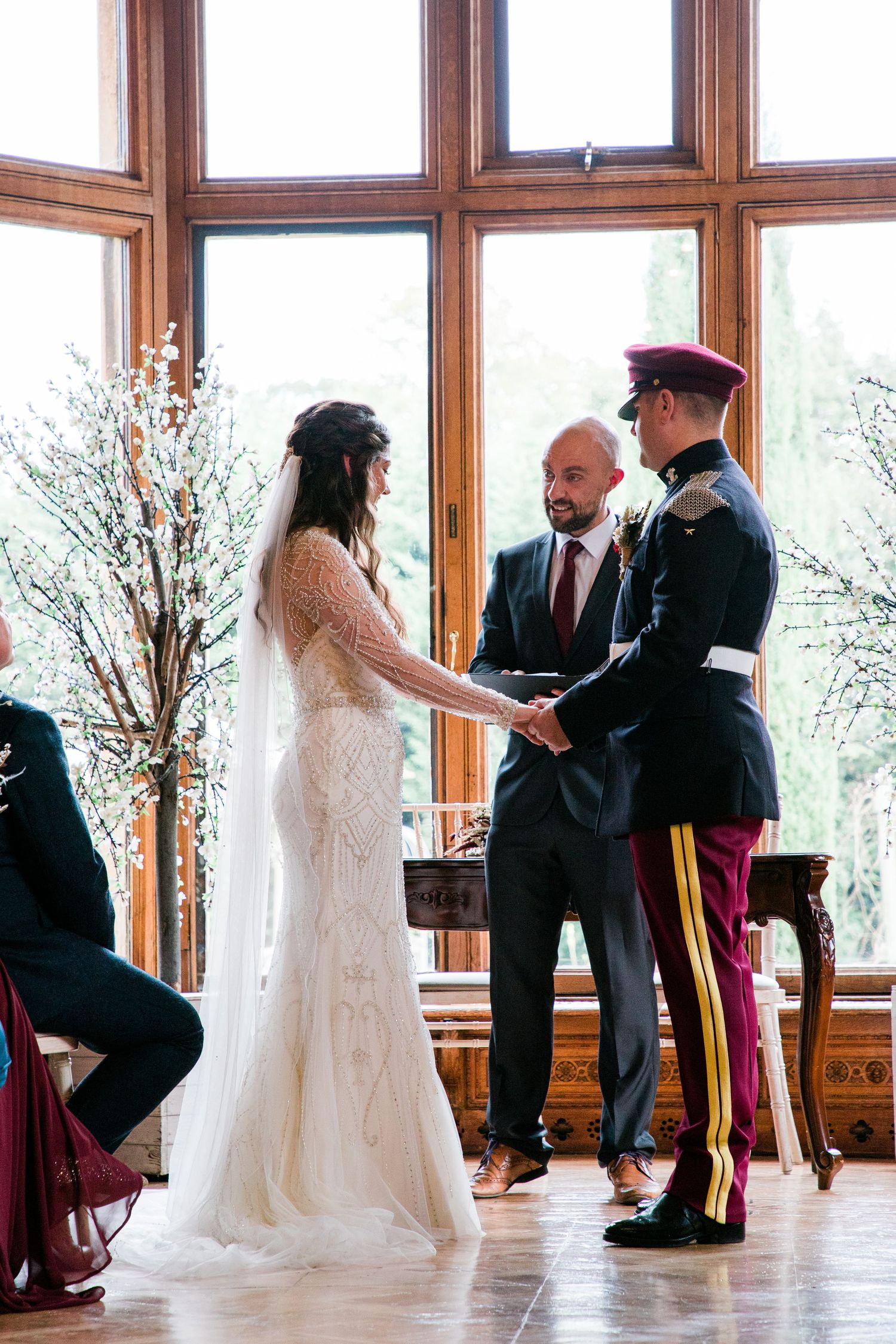 Wedding ceremony takes place in front of large windows in an elegant wood-paneled room.