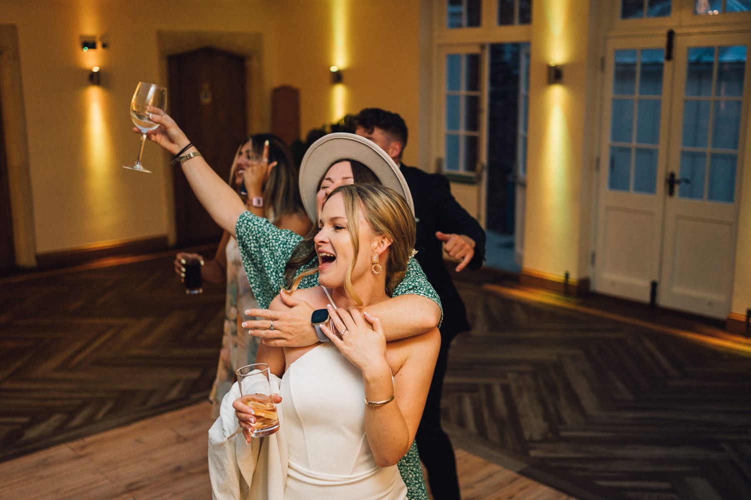 Wedding celebration in a grand ballroom with hardwood floors and ambient yellow lighting.
