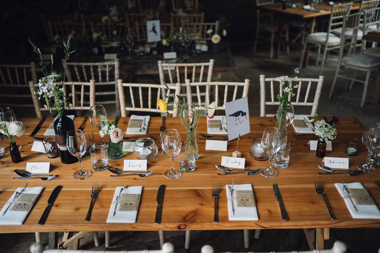 Rustic wooden tables set for a wedding reception with place settings and white chairs.