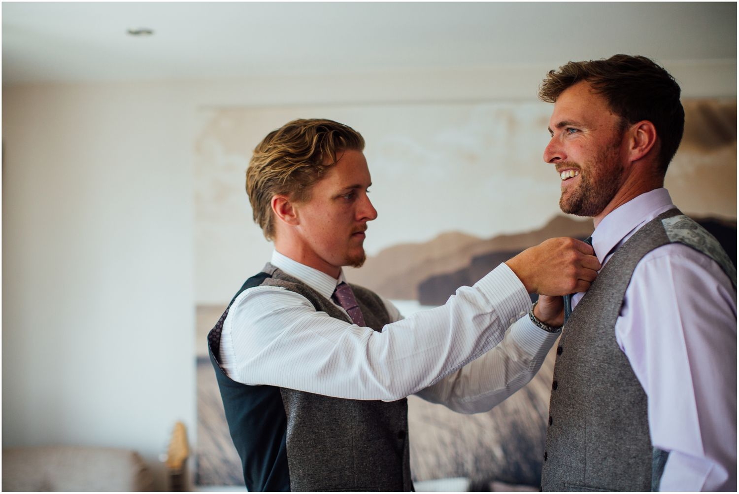 Two people in formal vests help each other with final wardrobe adjustments.