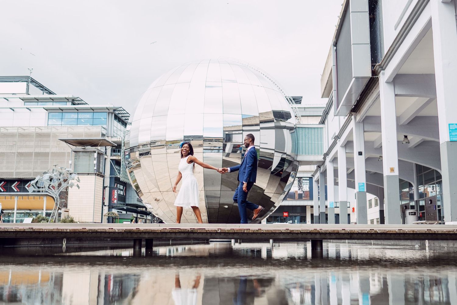 A couple poses beneath modern architectural structures and walkways.