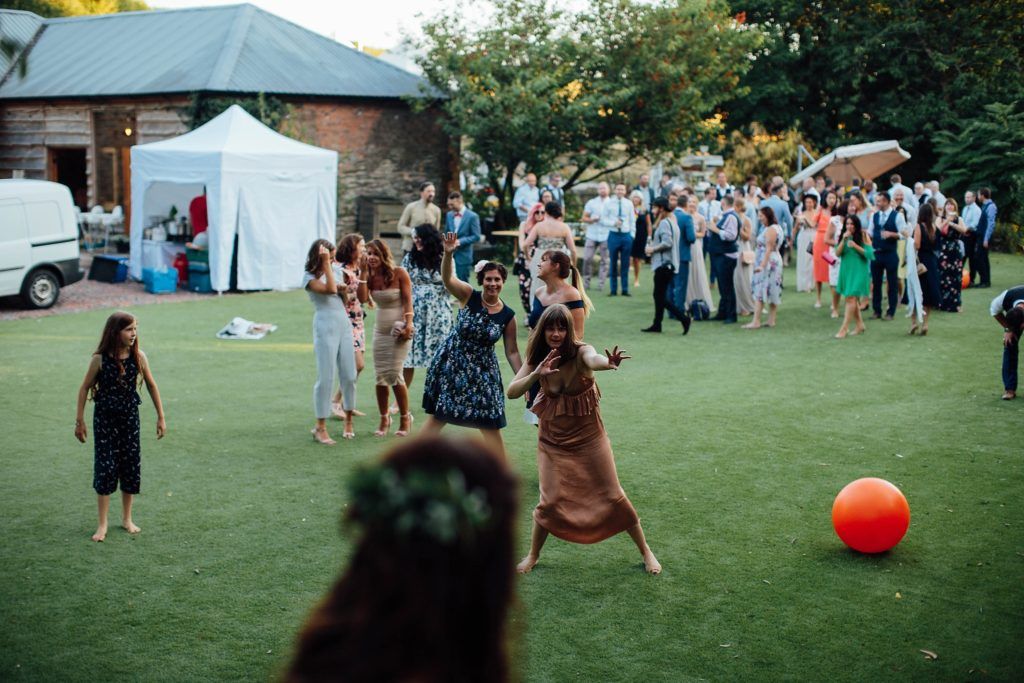 Wedding guests play outdoor games on a grassy lawn with white tents in the background.