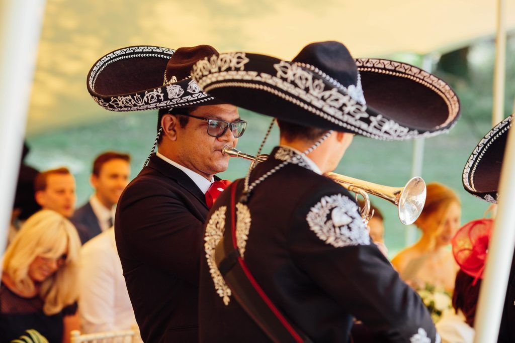 A mariachi band wearing traditional sombreros performs at an outdoor wedding celebration.