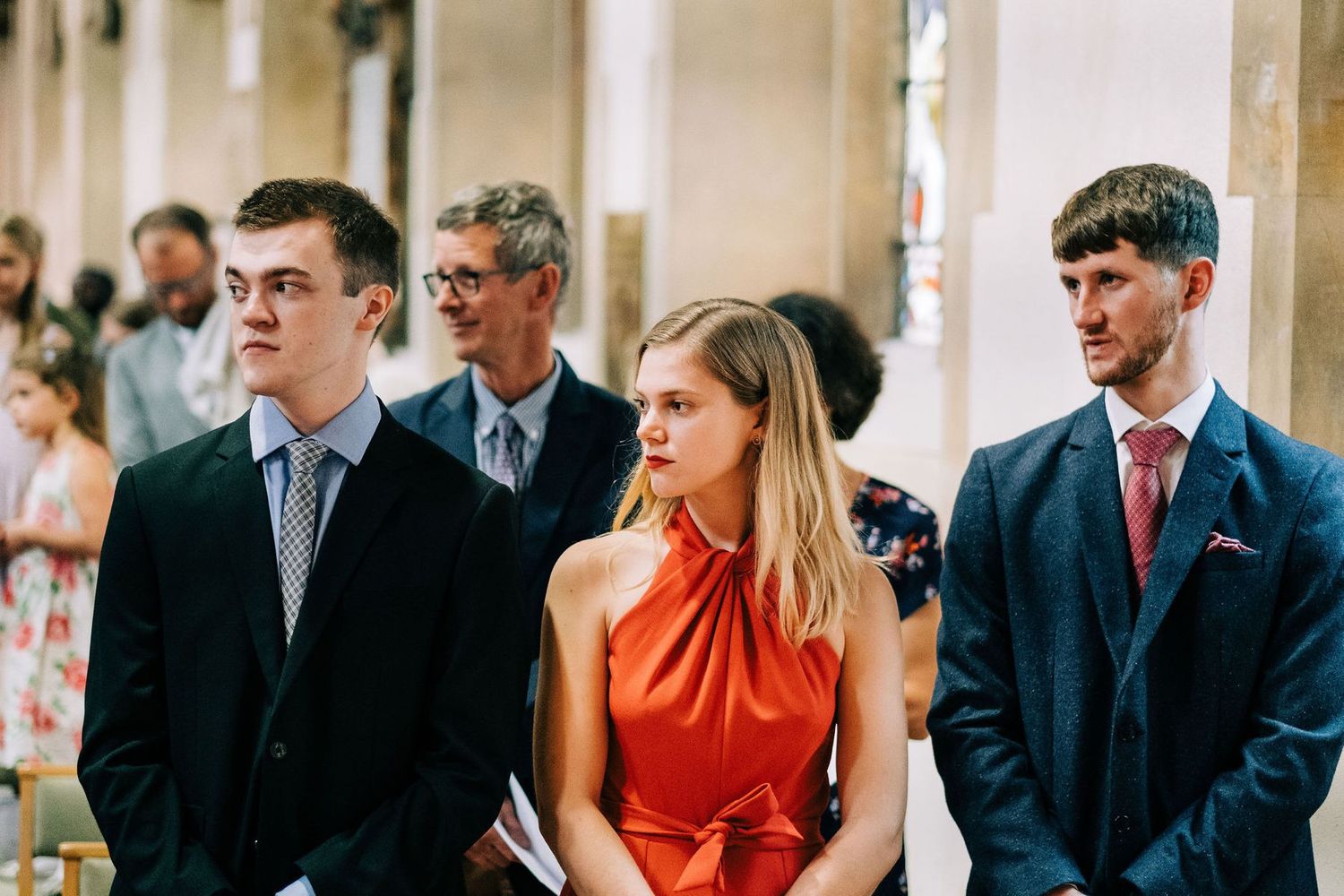 Wedding guests seated in church pews during ceremony, with one wearing a vibrant red dress.