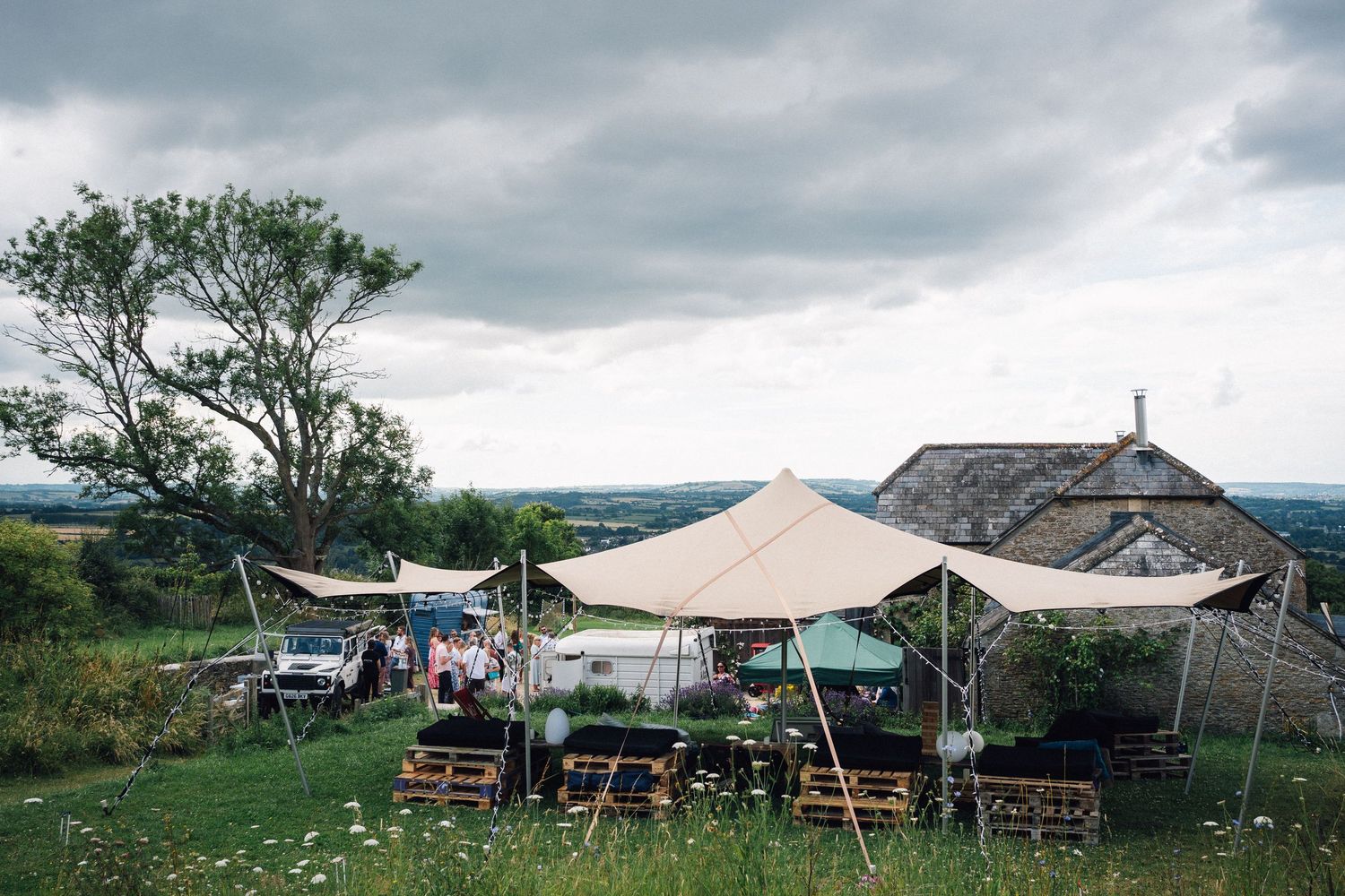 Outdoor wedding venue with white marquee tents set up against a cloudy countryside landscape.