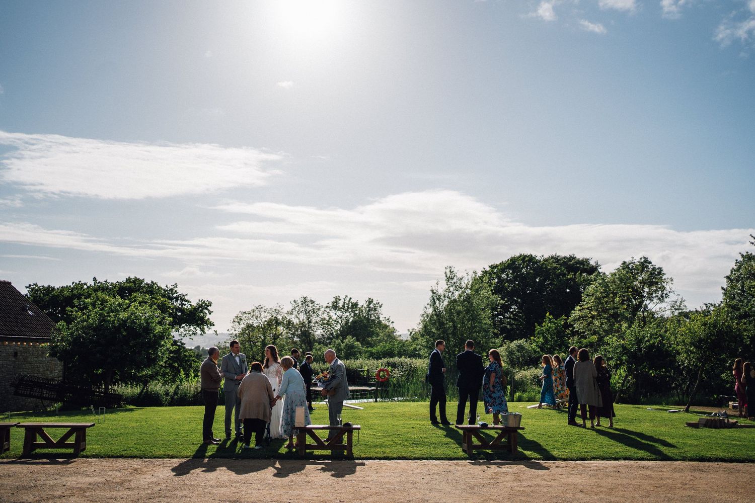Wedding guests silhouetted against bright sky in outdoor countryside setting.