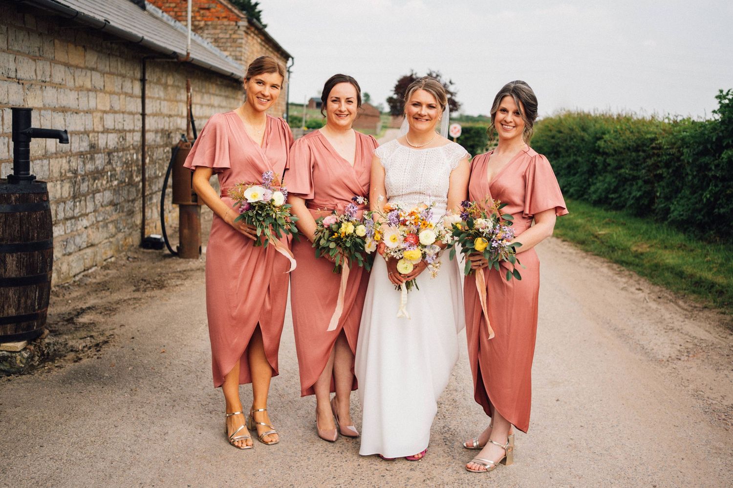 Wedding party in coral dresses poses together on a stone path.
