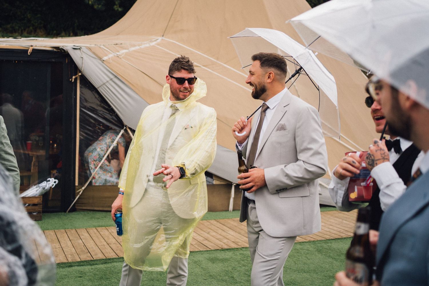 Guests in rain protection gear socializing outside teepee-style tents.
