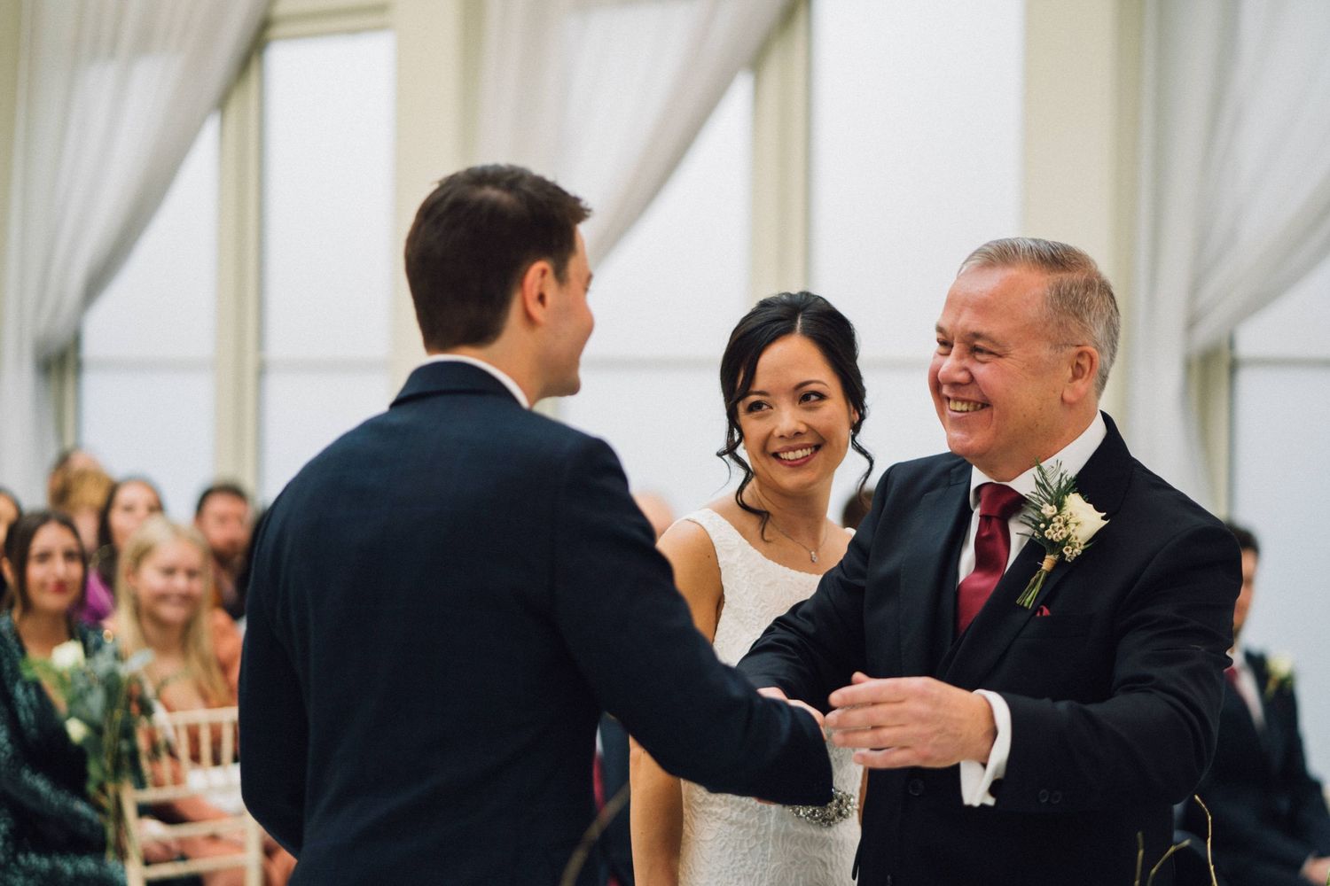 Elegant wedding ceremony taking place in a bright white room with guests watching the couple exchange vows.