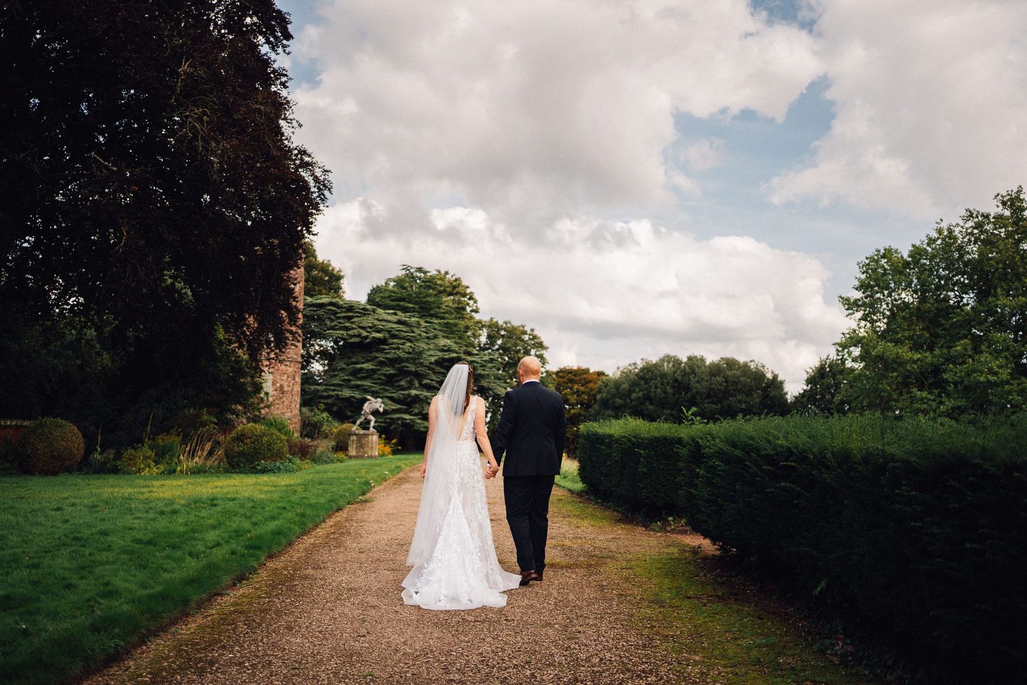 Wedding couple walking along a scenic countryside path with dramatic cloudy sky.