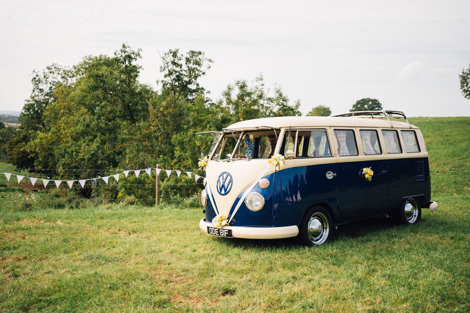 Vintage VW camper van in navy and cream parked on green grass with bunting decorations at an outdoor event.