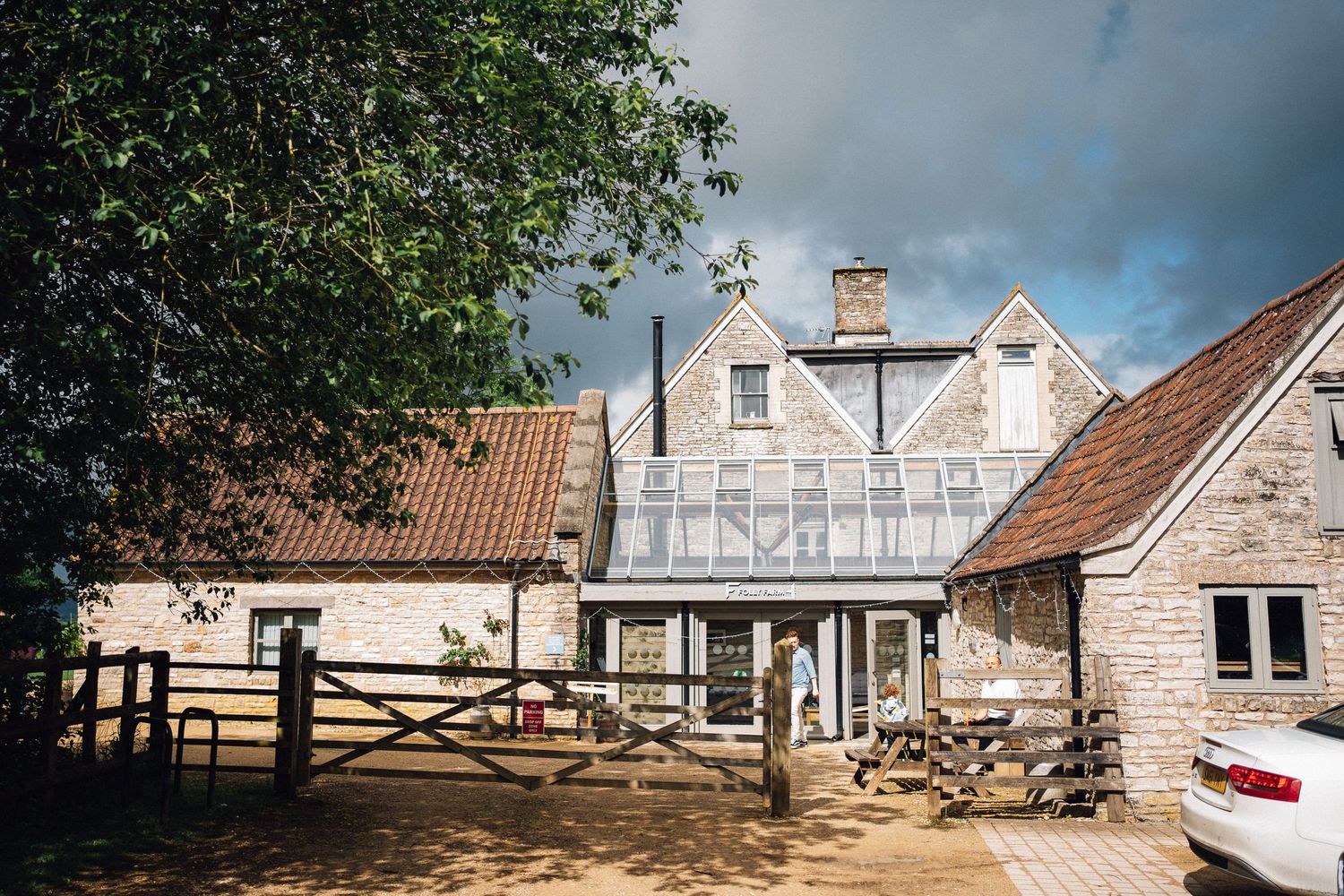 Rustic stone farmhouse with wooden gate, conservatory extension, and dramatic stormy sky in rural English countryside.