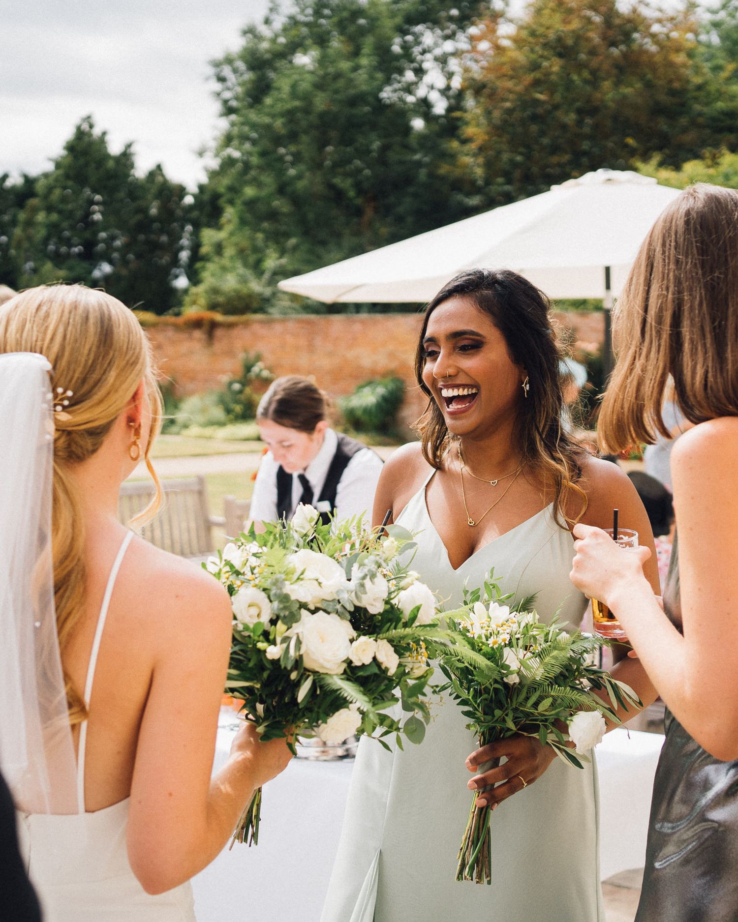 Wedding party members hold beautiful white and green floral bouquets while gathered outdoors.