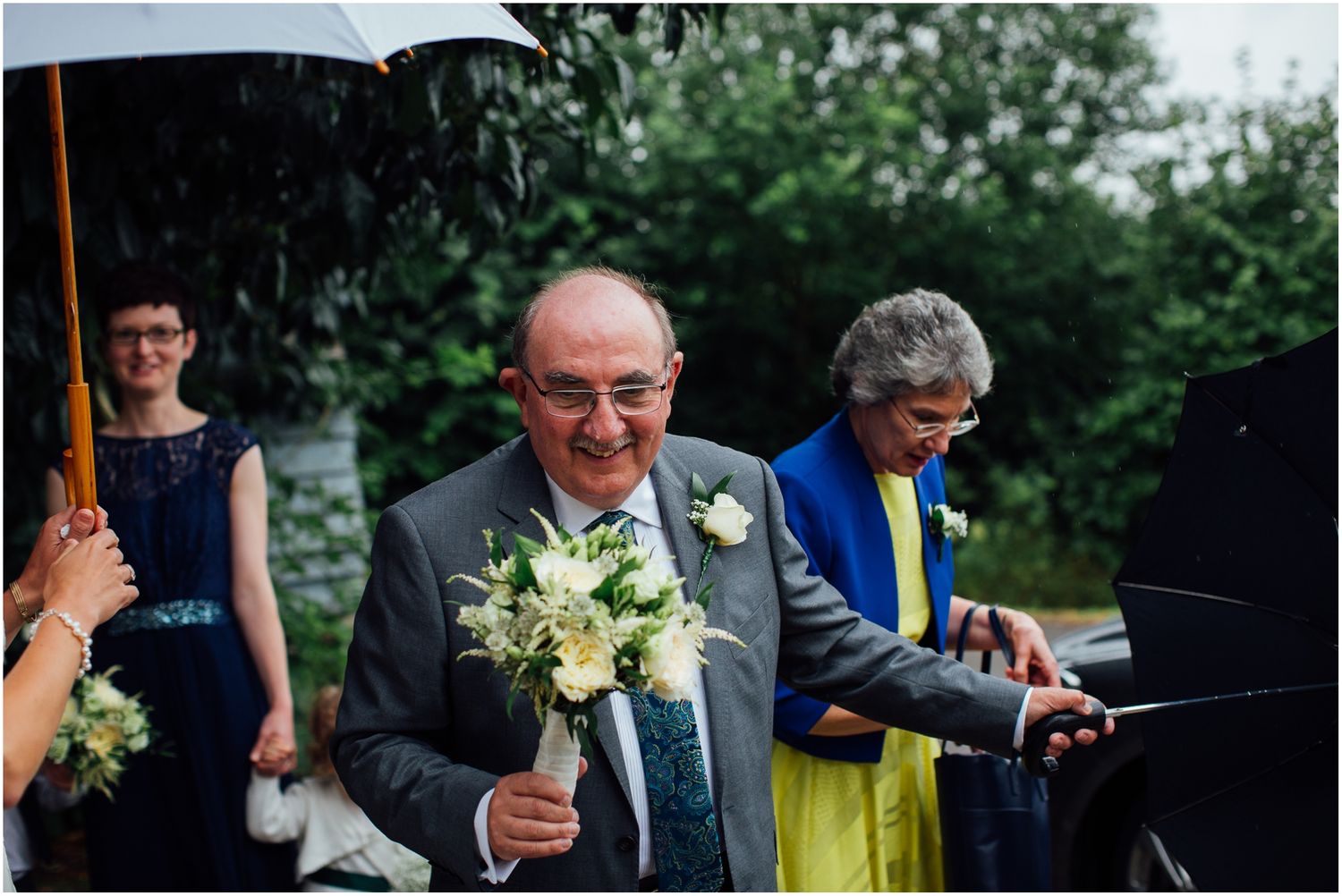 Wedding guests mingling outdoors with umbrellas during a rainy celebration.