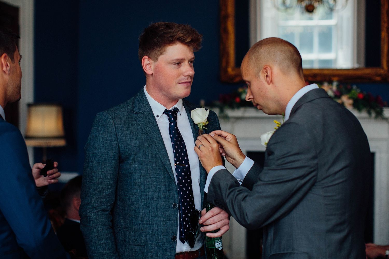 Wedding party members in formal attire enjoy drinks and conversation at an indoor reception.