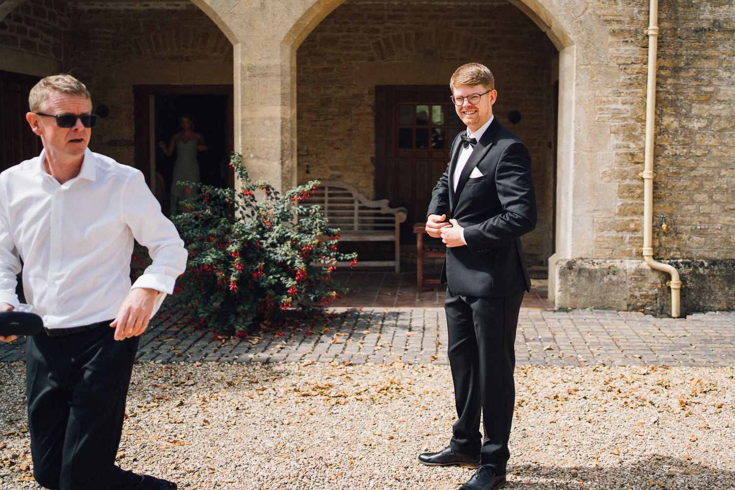 People in formal attire walking through stone archways of historic building.