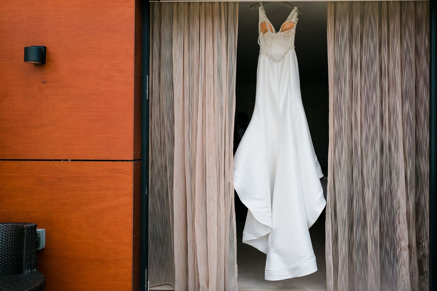White wedding dress hanging elegantly against wooden paneled walls with soft curtains.