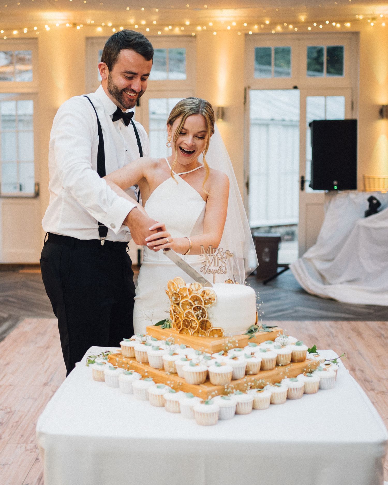 A couple cuts their wedding cake decorated with cupcakes at their reception.