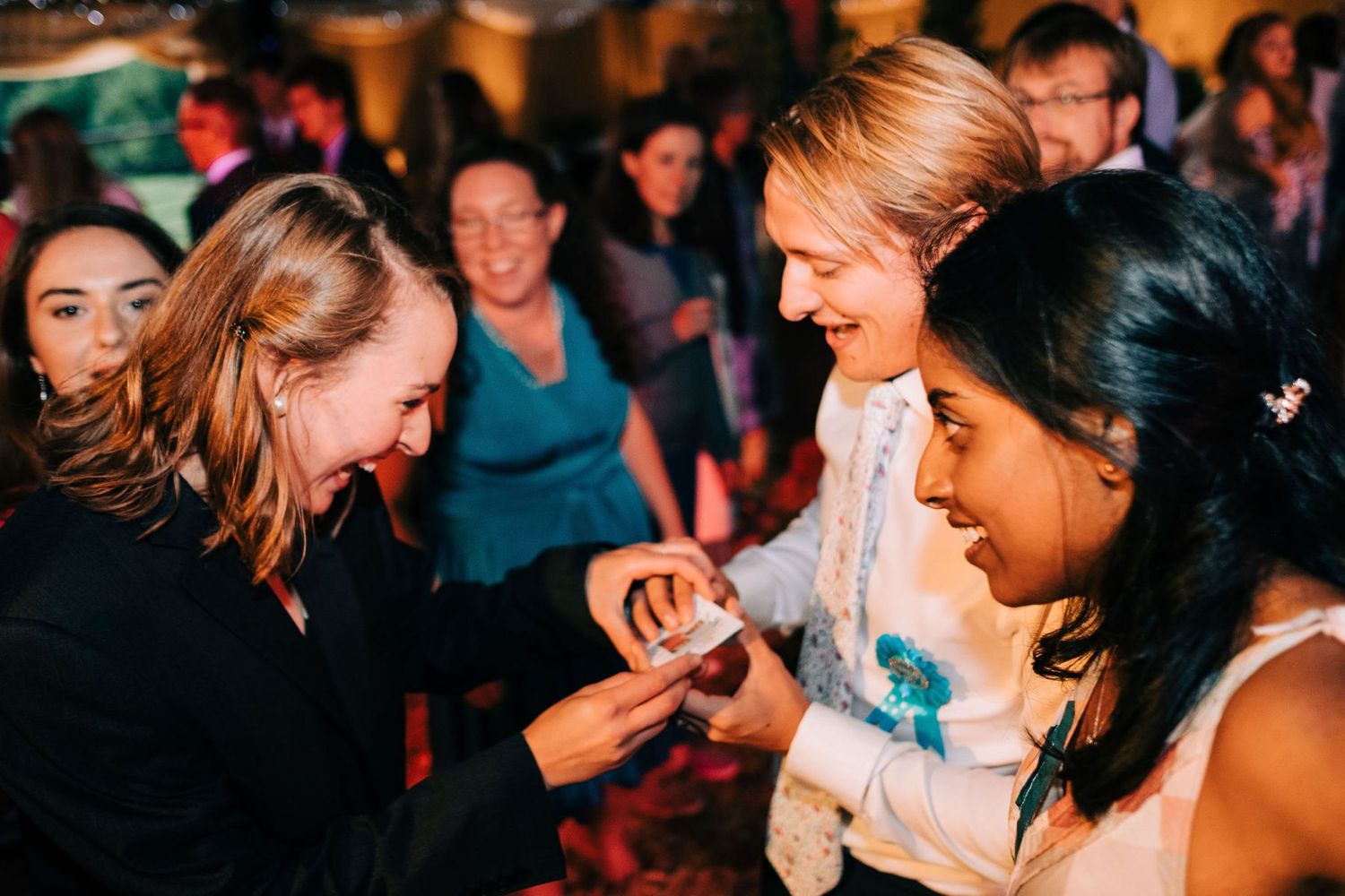 Wedding reception guests dancing and celebrating together in a dimly lit venue.