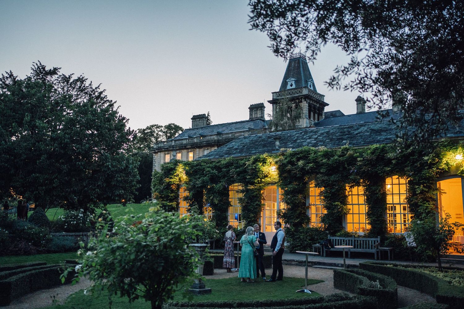 Evening exterior view of an elegant venue with glowing windows and landscaped gardens.