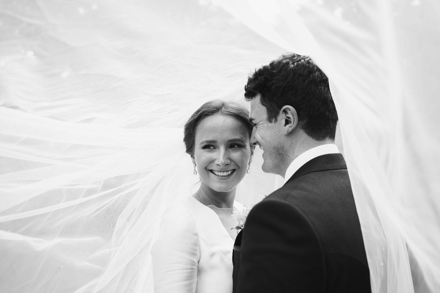 Romantic black and white wedding portrait with flowing veil detail.