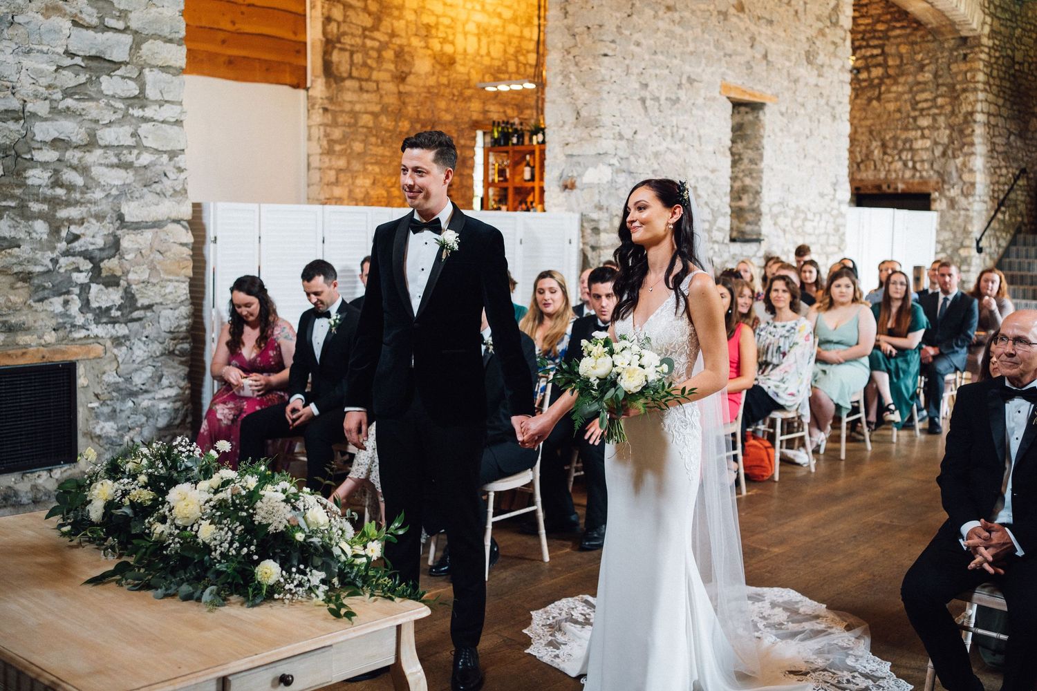 Wedding reception in rustic stone barn with elegant floral decorations and seated guests.