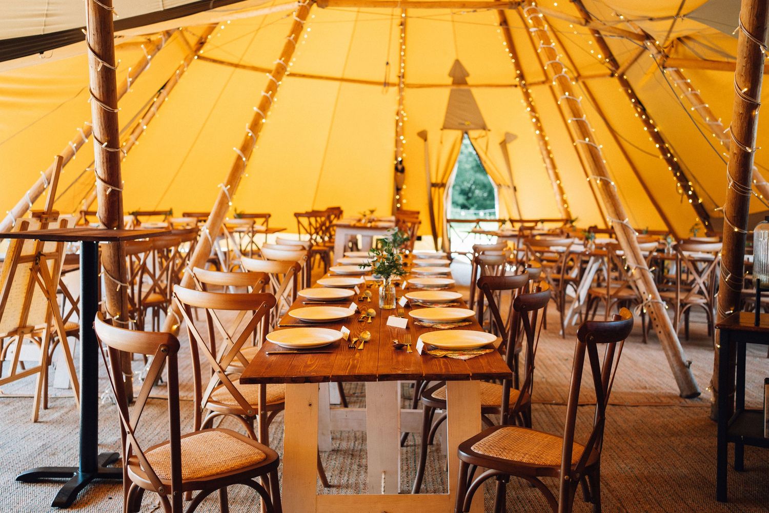 Interior view of a tipi tent set up for dining with tables and chairs arranged in rows.